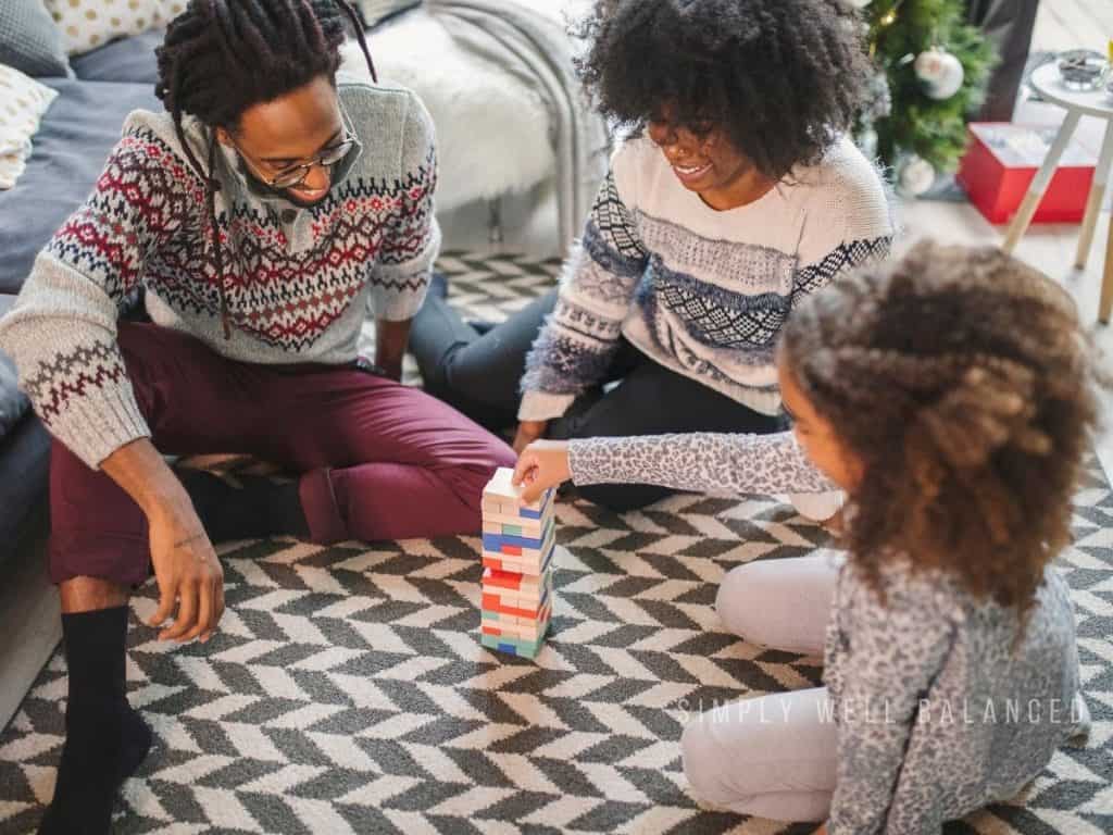 Parents and child playing Jenga-style blocks during a cozy family night at home.