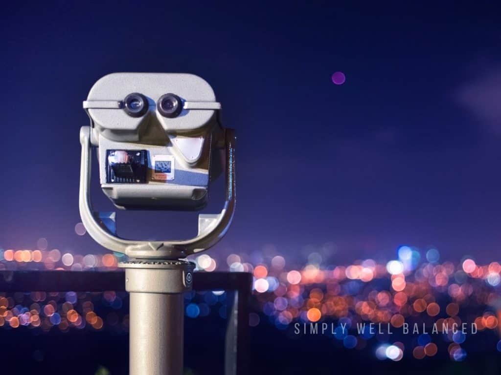 Coin-operated binocular viewer overlooking a city skyline at night.