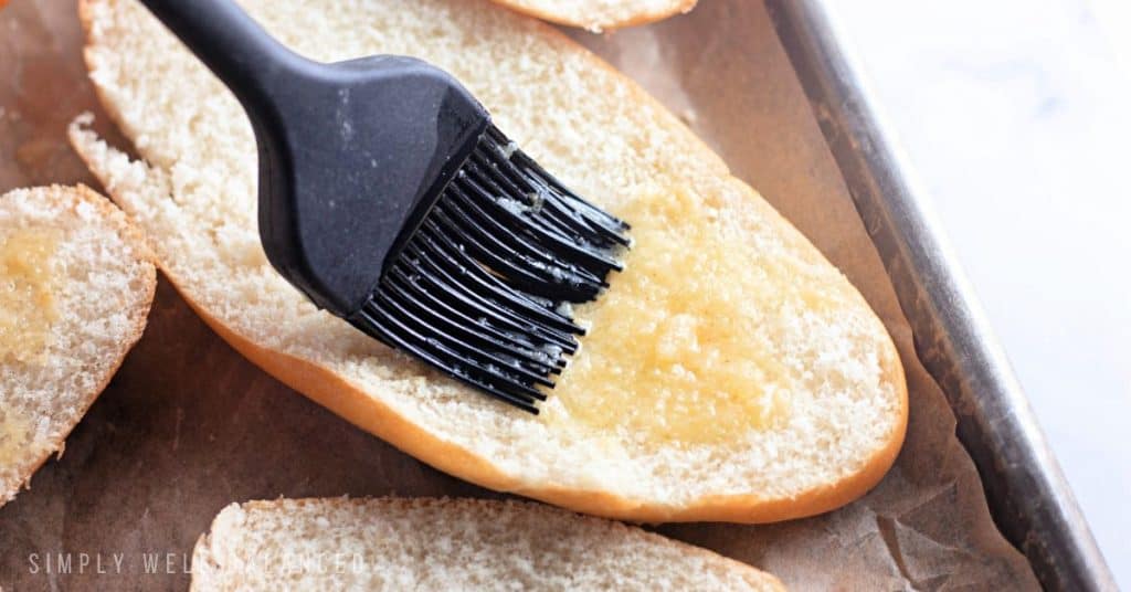 Brushing garlic butter on rolls to bake for spaghetti bread. 