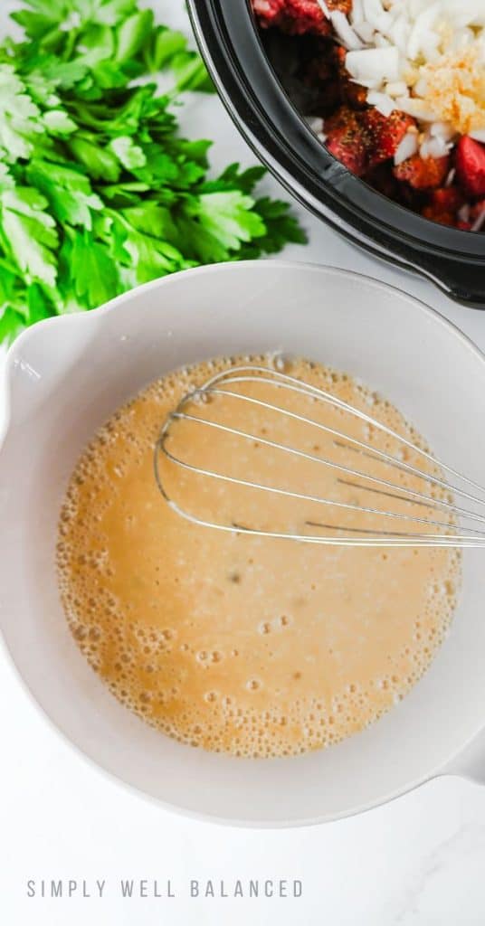 Slow Cooker Beef Stroganoff Recipe Step 2: Worcestershire sauce, mushroom soup and beef broth in a white bowl with a whisk to mix it all together.